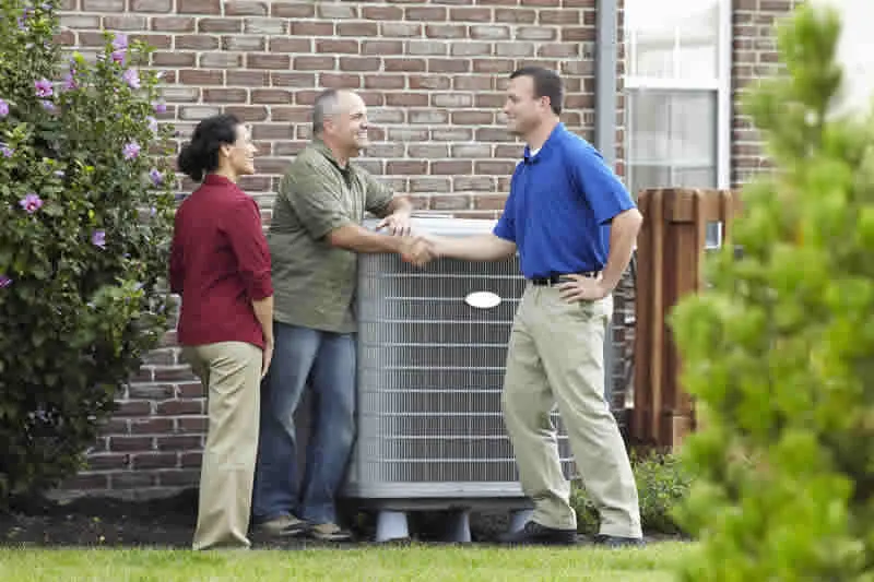 Technician shaking hands with homeowners beside an outdoor AC unit