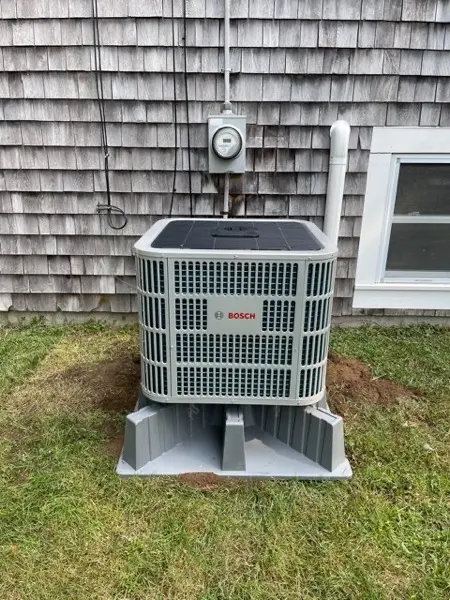 Outdoor heat pump condenser beside a shingled wall
